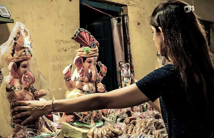 Welcoming devotion with care: a young woman gently arranges beautifully crafted Lord Ganesha idols, preparing to bring festive blessings home for Ganesh Chaturthi.