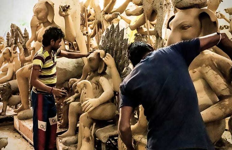 Shaping faith from the ground up: artisans work side-by-side in a bustling workshop, meticulously sculpting raw clay into majestic idols of Lord Ganesha in preparation for Ganesh Chaturthi.