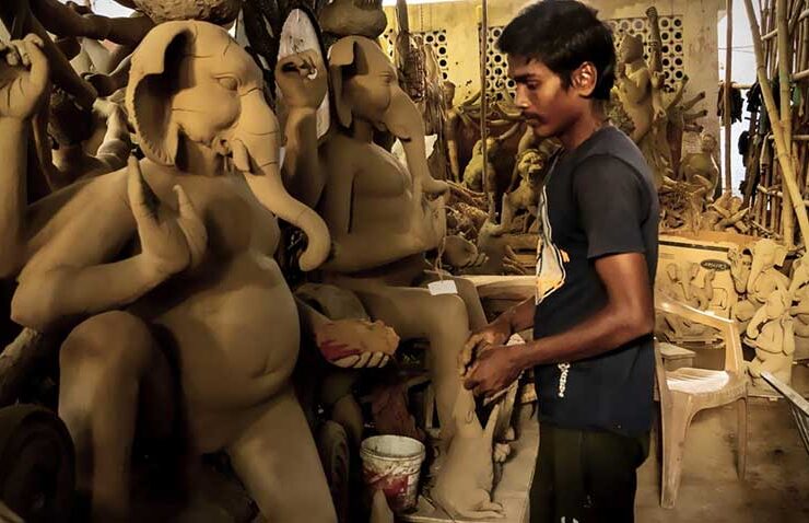 Crafting devotion with patience and precision. A young artisan works attentively on a small clay figure, surrounded by large, beautifully sculpted idols of Lord Ganesha taking shape in a traditional workshop ahead of the festive season.